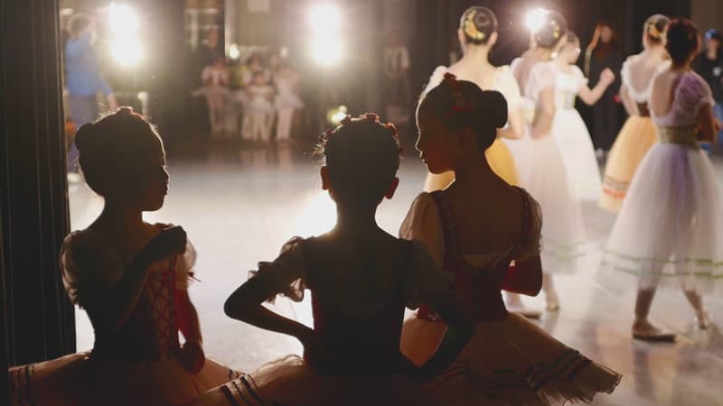 Young ballet dancers in tutus watching the stage from the wings at a recital